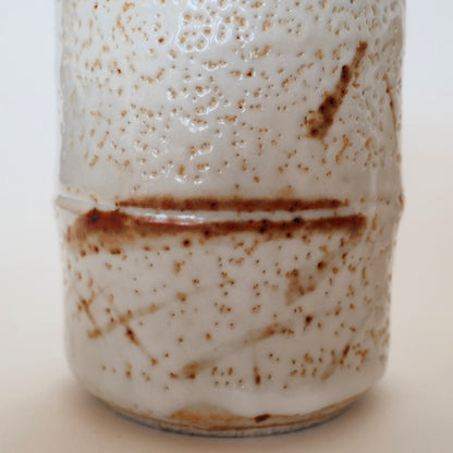 Zoom sur la surface d’une tasse japonaise Shino-yaki montrant la glaçure à effet de neige et les motifs brun rouge.