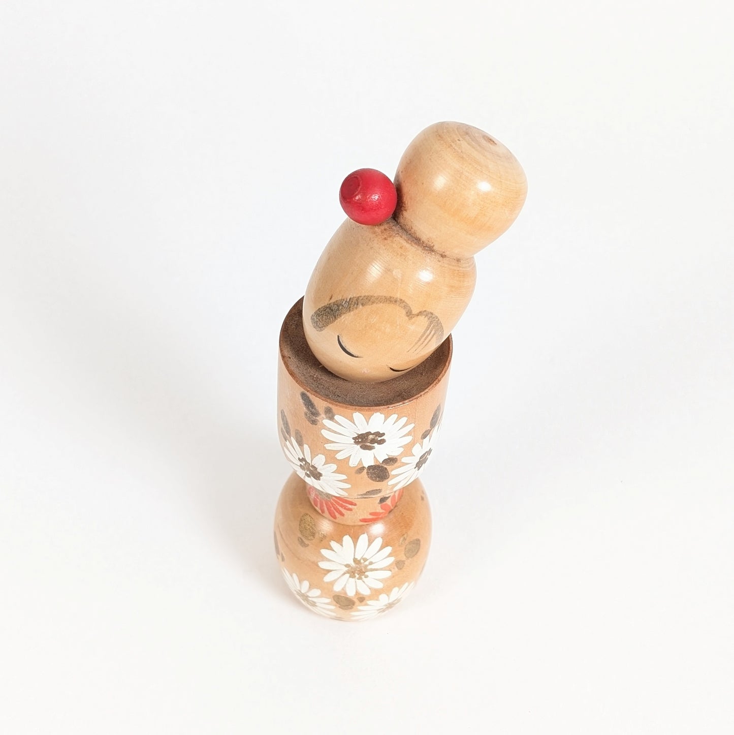 Vue du dessus d’une kokeshi d’artiste japonais par Ishida Tomio, avec chignon rouge et motifs floraux.