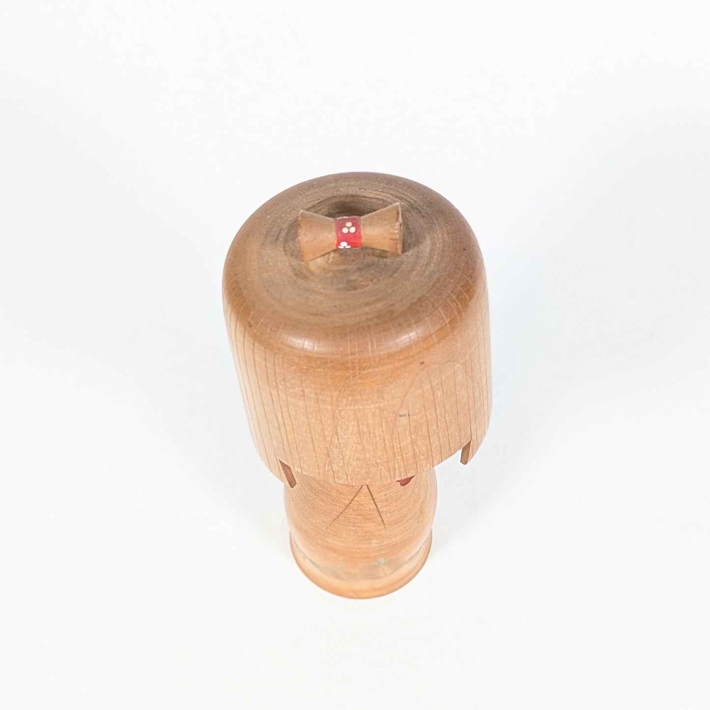 Kokeshi authentique du Japon de style sōsaku, vue du dessus sur le chignon en bois et le ruban rouge à pois blancs