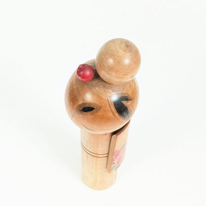 Vue du dessus de la coiffure d'une kokeshi japonaise sosaku avec chignon rond et petit ornement kanzashi rouge