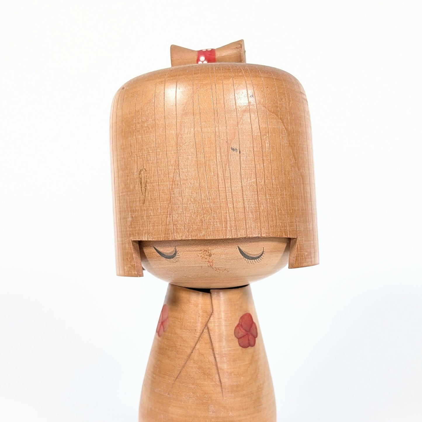 Kokeshi créative japonaise par Izumi Ueda, gros plan sur le visage paisible aux yeux clos et la coiffure géométrique sculptée