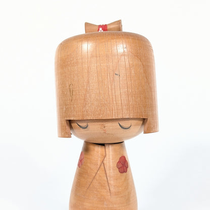 Kokeshi créative japonaise par Izumi Ueda, gros plan sur le visage paisible aux yeux clos et la coiffure géométrique sculptée