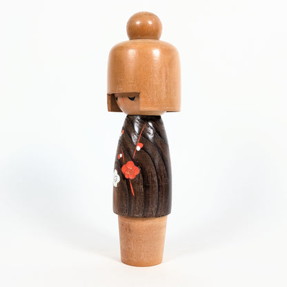 Kokeshi créative japonaise de type sōsaku, modèle Koigokoro d'Usaburo, vue de profil avec un kimono brun foncé orné de fleurs rouges et blanches.