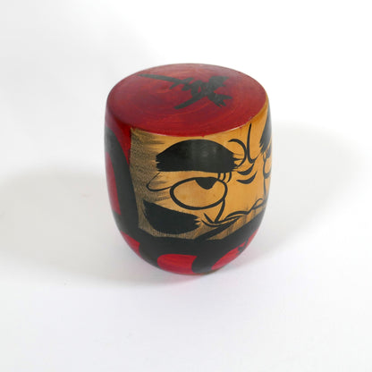 Profil d’une kokeshi Daruma artisanale au regard intense et peinture brossée