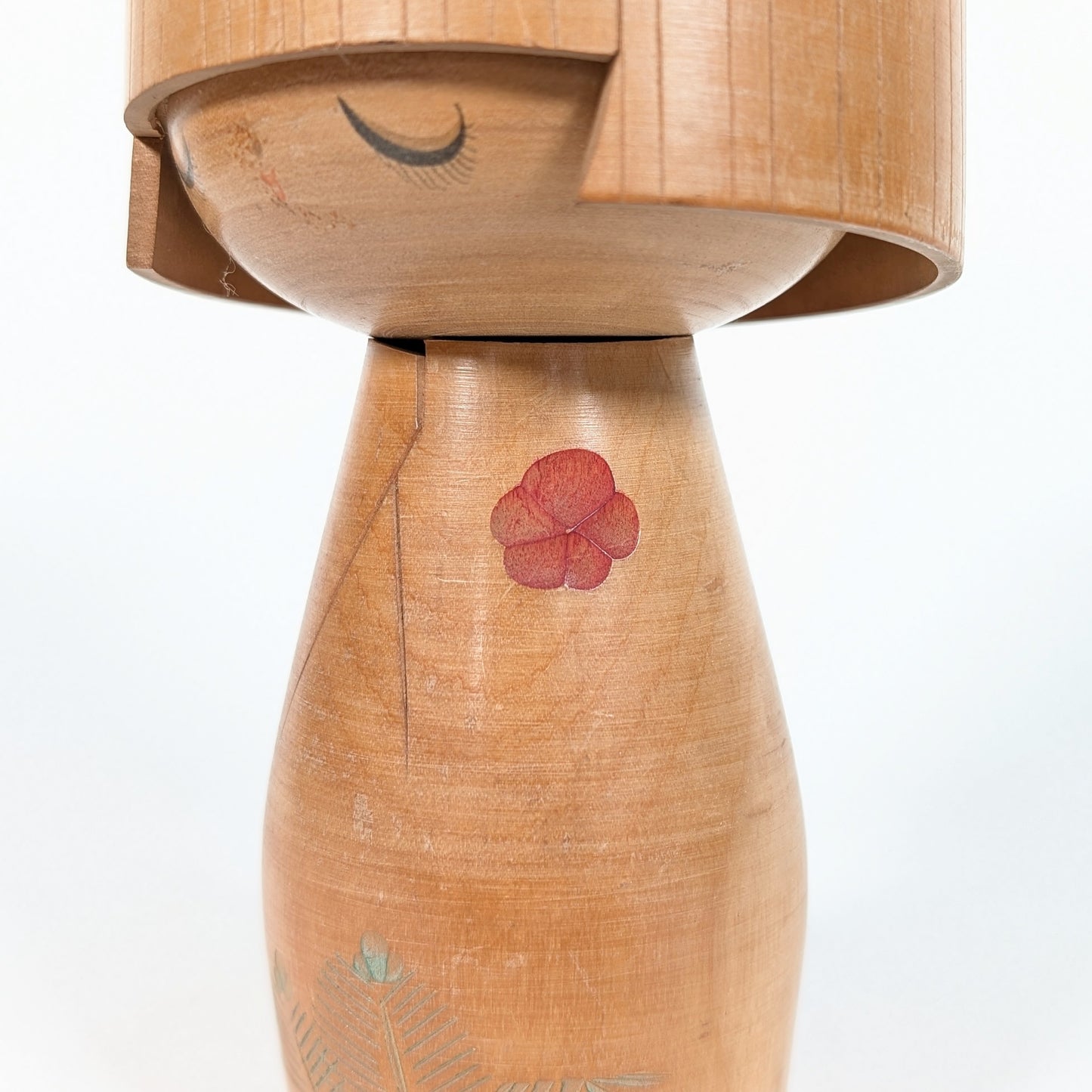 Kokeshi de collection signée Ueda Izumi, détail de profil avec visage aux yeux fermés, fleur rouge et bois patiné