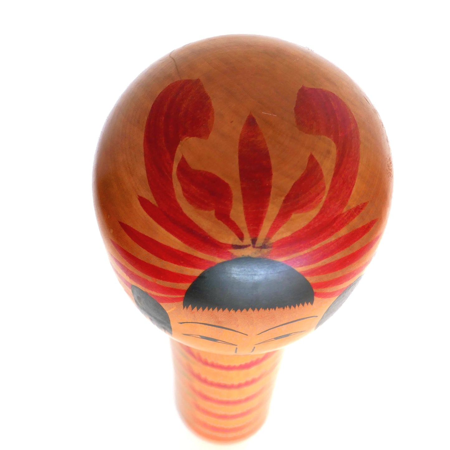 Vue du dessus d’une kokeshi Hijiori montrant le motif Tegara rouge sur la tête, symbole décoratif typique