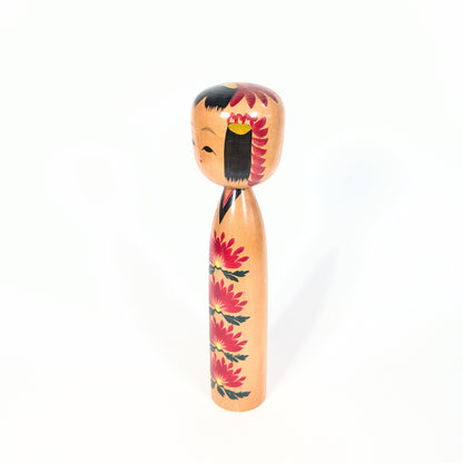 Profil d’une kokeshi japonaise shingata avec visage doux, cheveux noirs peints et décor kasane giku sur la tête et le corps.