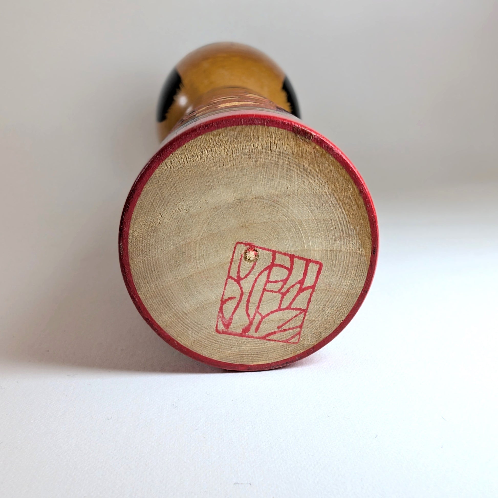 Signature rouge sous la base d’une kokeshi japonaise vintage en bois, œuvre de Sasaki Katsumi