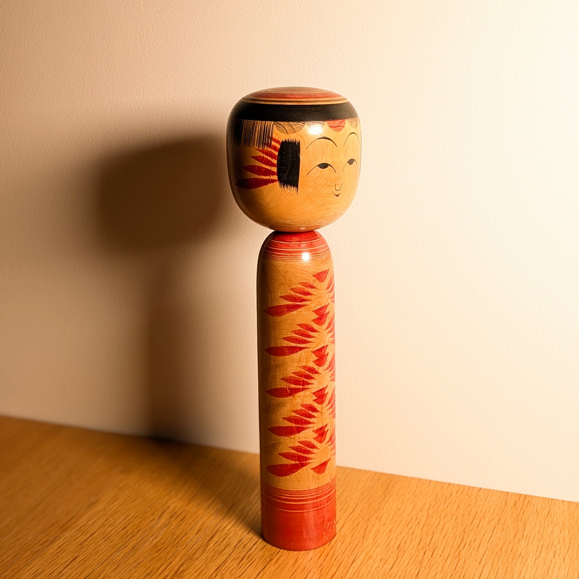 Grande kokeshi japonaise traditionnelle Yajirō par Kamata Kōichi, décor rouge chrysanthèmes kasane-giku, photographiée en lumière naturelle.