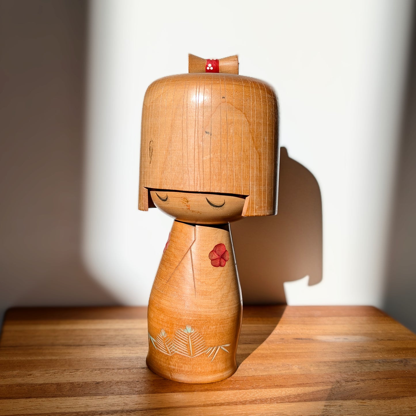 Kokeshi japonaise vintage Hōshun par Ueda Izumi, poupée sōsaku en bois exposée en lumière naturelle avec ombre décorative sur meuble en bois