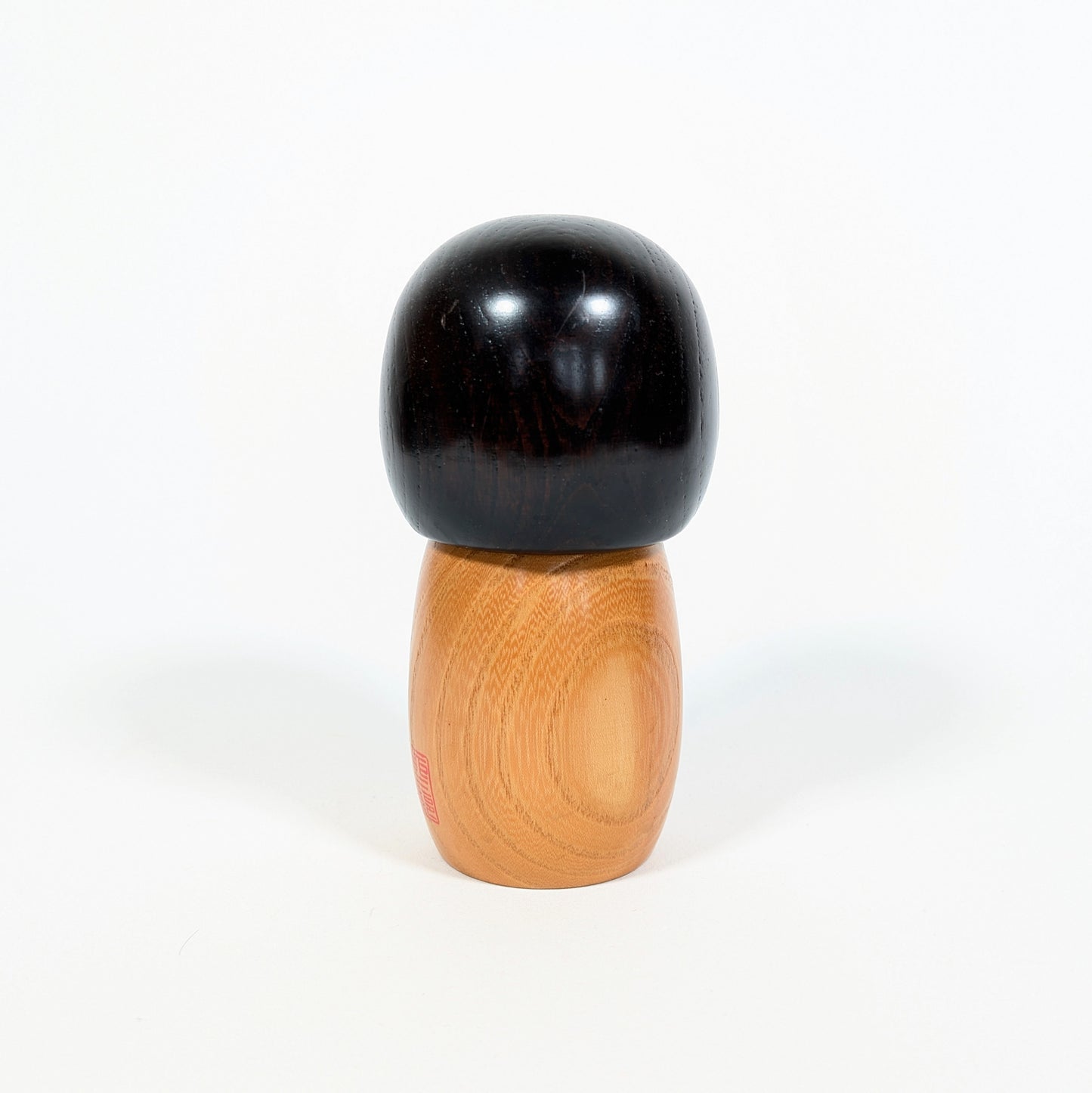 Dos d’une kokeshi japonaise Usaburo Haru no uta montrant le bois naturel veiné et la chevelure noire laquée