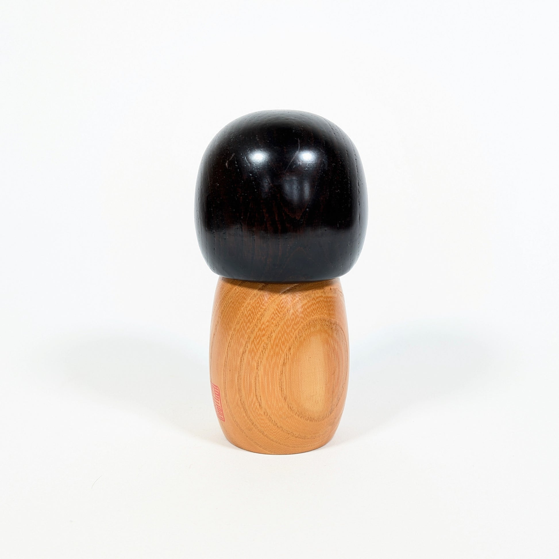 Dos d’une kokeshi japonaise Usaburo Haru no uta montrant le bois naturel veiné et la chevelure noire laquée