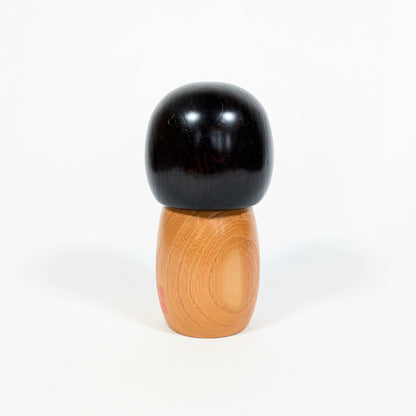 Dos d’une kokeshi japonaise Usaburo Haru no uta montrant le bois naturel veiné et la chevelure noire laquée
