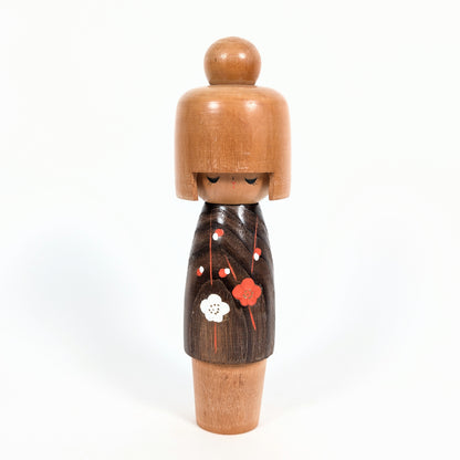 Kokeshi japonaise Koigokoro de l'atelier Usaburo, vue de face avec coiffure en bois clair et kimono brun décoré de fleurs de prunier rouges et blanches.