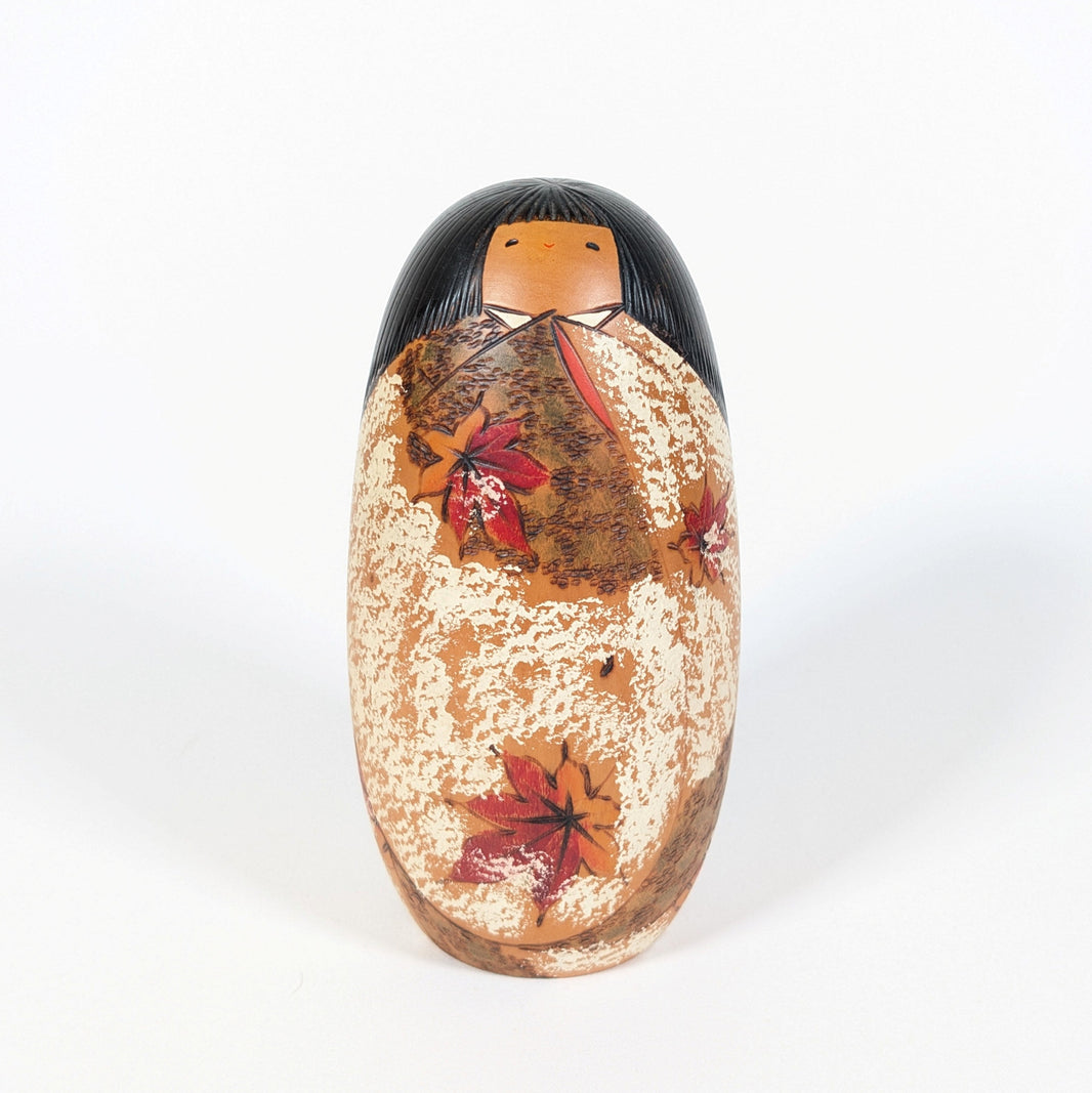 Vue de face de la kokeshi Usaburo Shôzan de 16 cm, poupée japonaise en bois au kimono ocre et crème décoré de feuilles d’érable rouges.