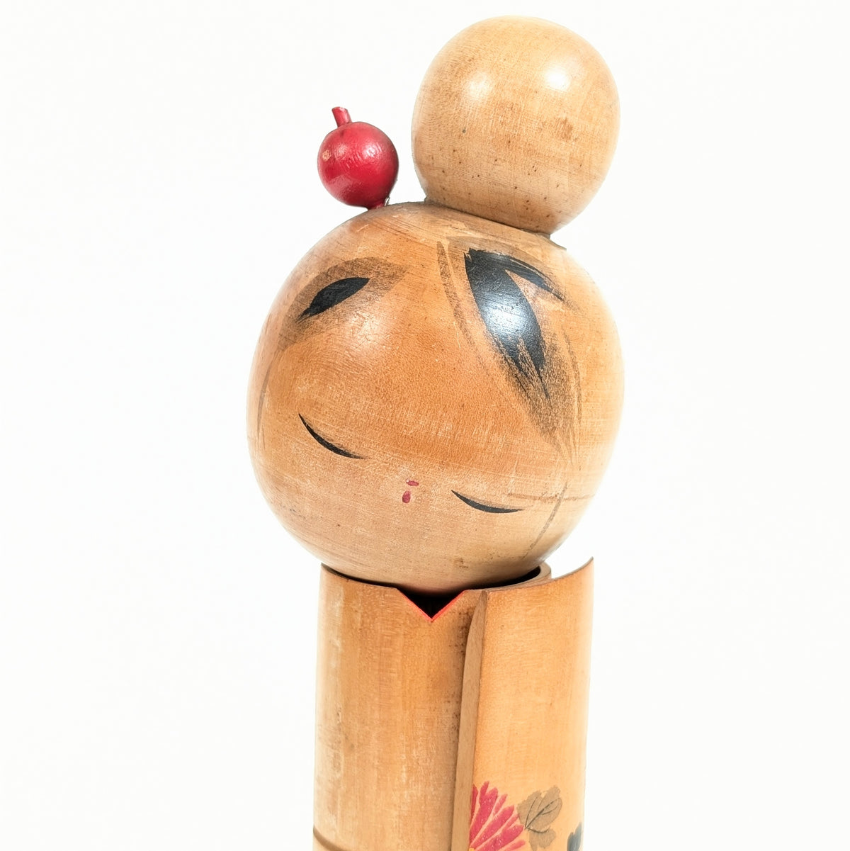 Gros plan du visage serein d'une poupée  kokeshi japonaise, yeux baissés, chignon traditionnel et kanzashi rouge