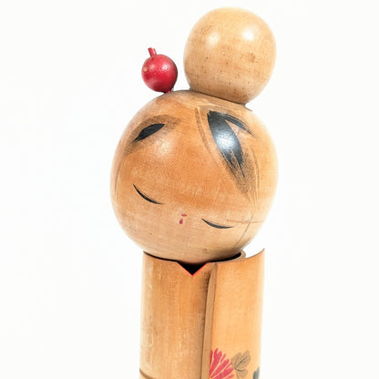 Gros plan du visage serein d'une poupée  kokeshi japonaise, yeux baissés, chignon traditionnel et kanzashi rouge
