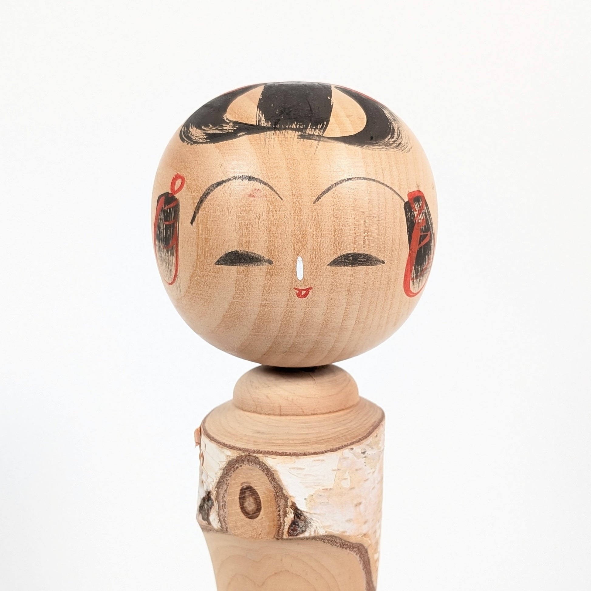 Visage peint d’une kokeshi japonaise en bois, expression souriante, coiffure traditionnelle noire et détails rouges