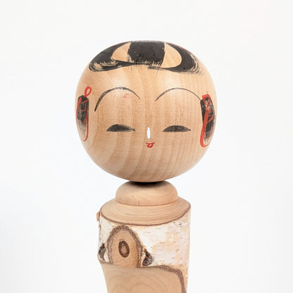 Visage peint d’une kokeshi japonaise en bois, expression souriante, coiffure traditionnelle noire et détails rouges