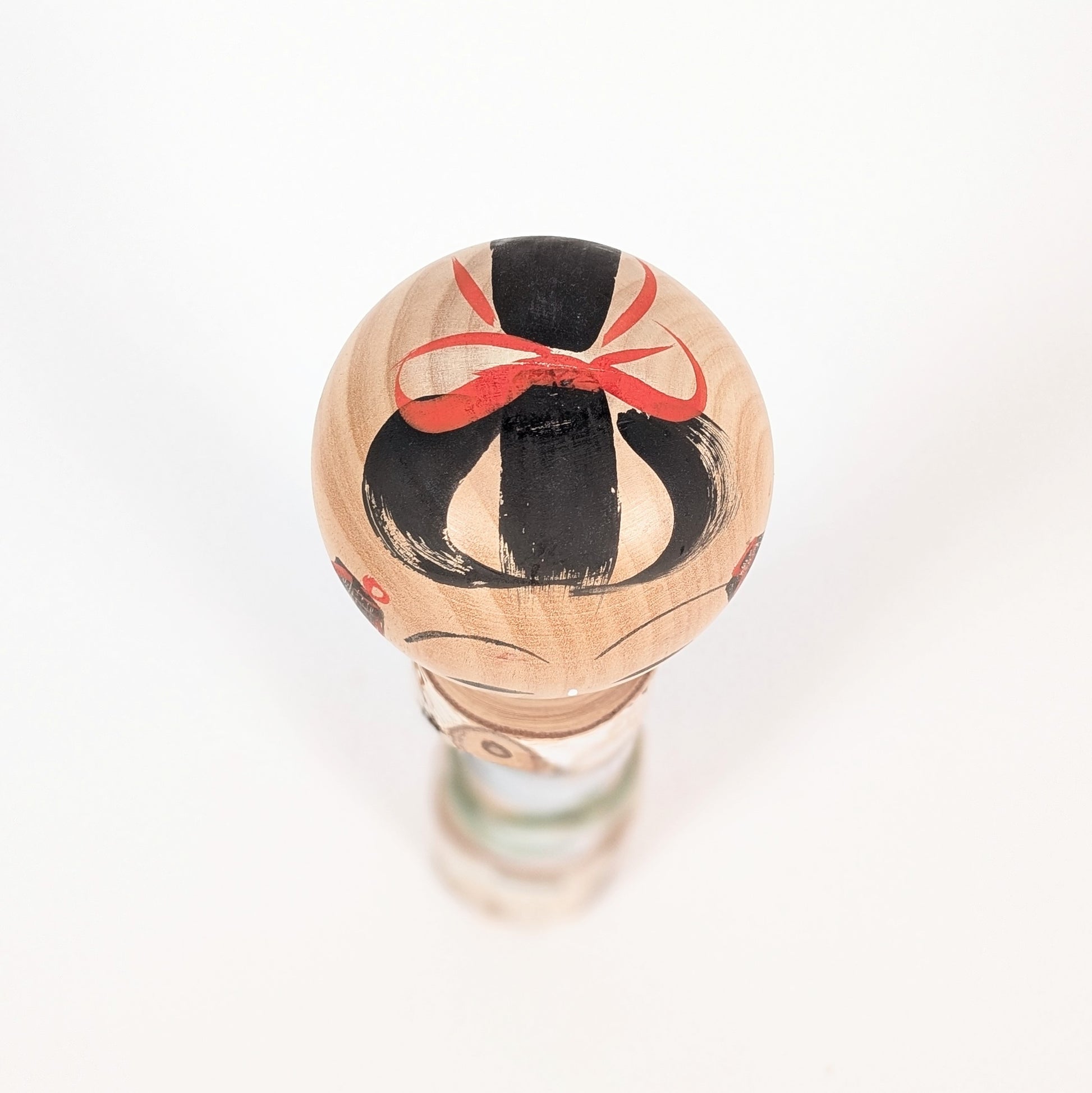 Vue du dessus d’une kokeshi japonaise au visage souriant, coiffure noire et rouge peinte à la main