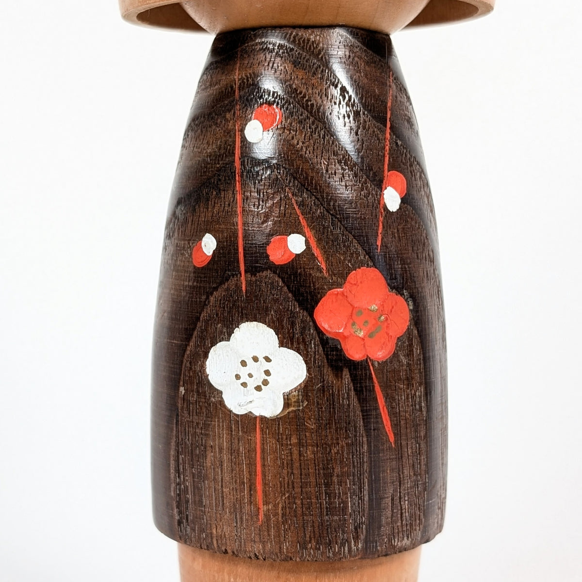 Détail du kimono brun de la kokeshi Koigokoro, décoré de fleurs de prunier japonais ume rouges et blanches, peintes en relief sur le bois au veinage apparent.