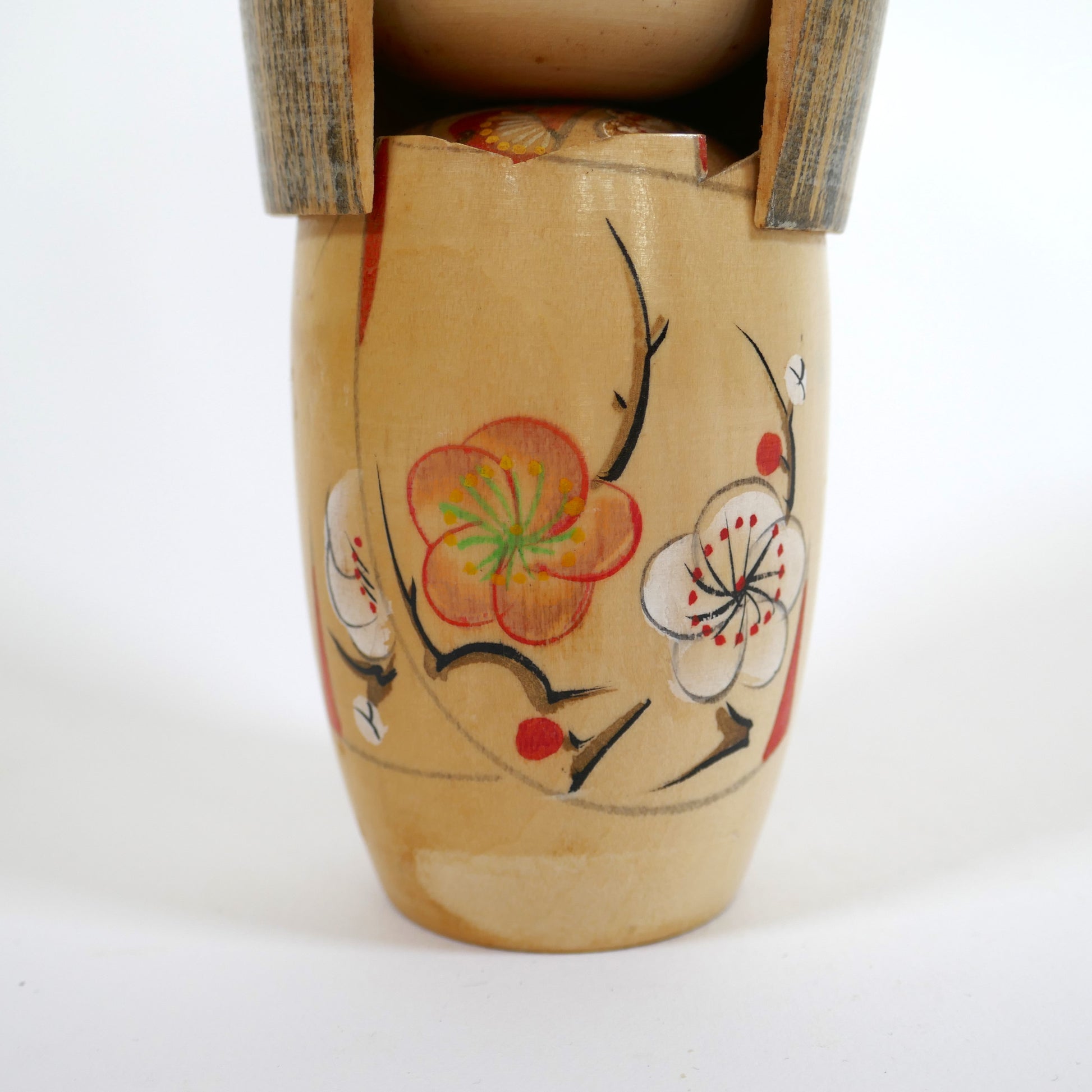 Détail gros plan des fleurs de prunier (ume) peintes à la main sur la kokeshi créative de Kojo Tanaka.