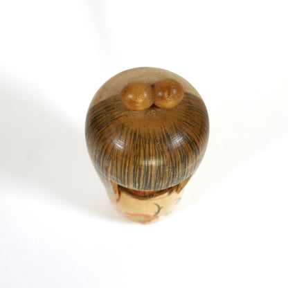 Vue de dessus de la kokeshi Kojo Tanaka : chignon à deux boules et chevelure peinte, poupée kokeshi sosaku.