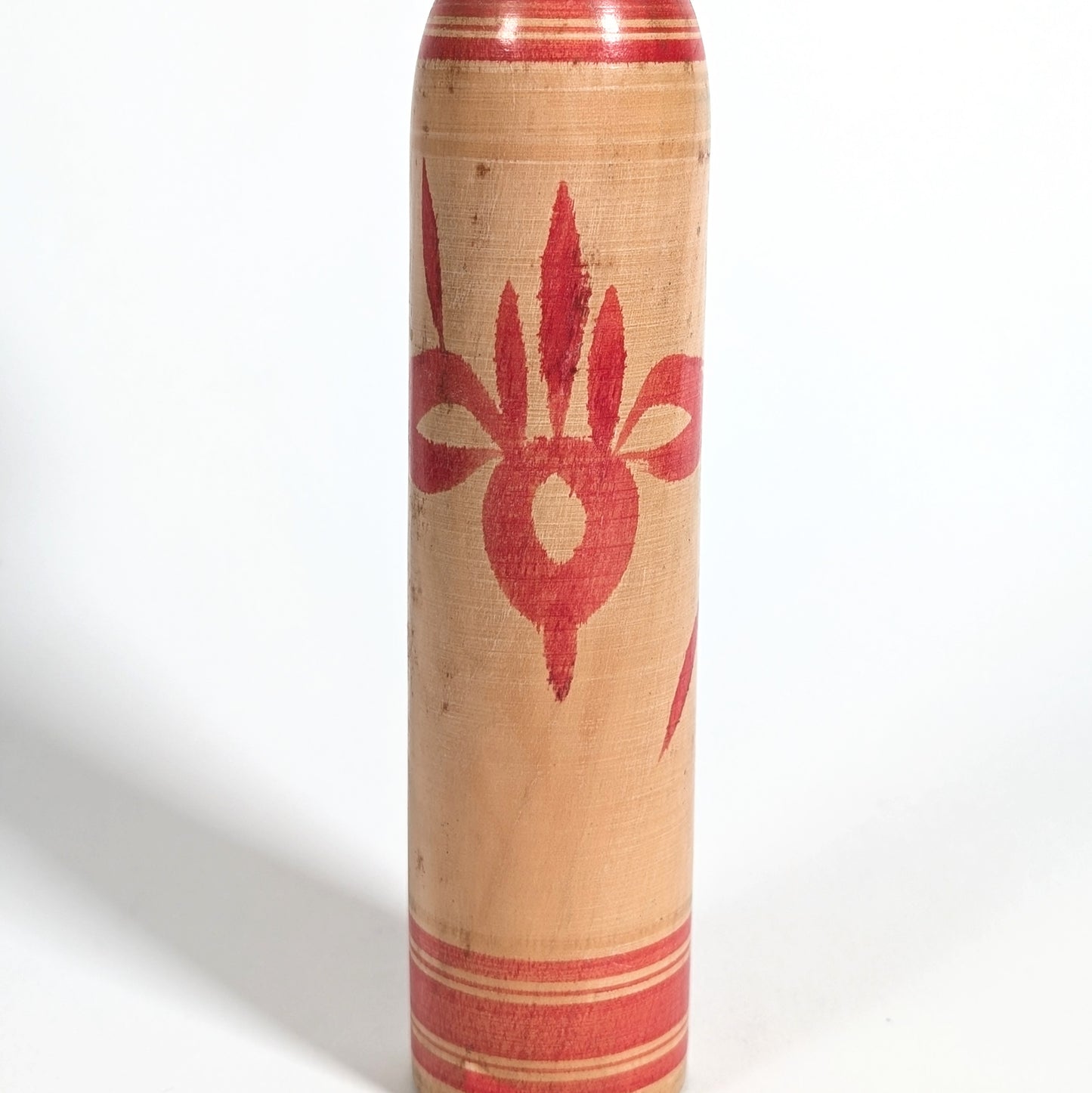 Détail du motif iris rouge peint à la main sur une kokeshi japonaise artisanale de style Tsuchiyu.