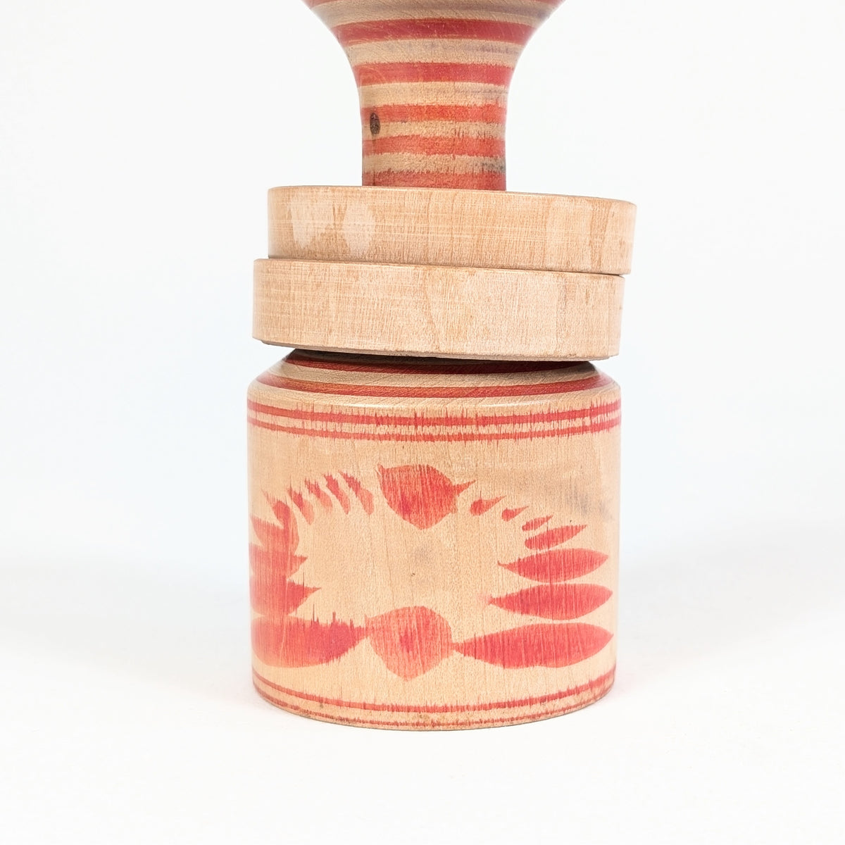 Détail de la base en bois tourné de la kokeshi Nagao Masayoshi, ornée d’un motif floral rouge de type kiku.