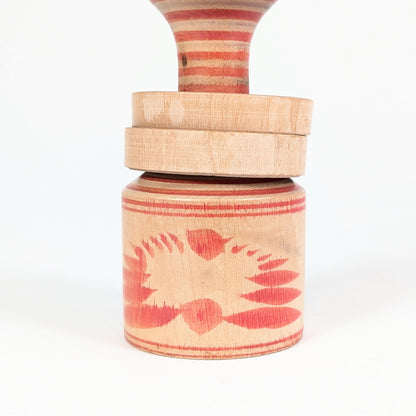 Détail de la base en bois tourné de la kokeshi Nagao Masayoshi, ornée d’un motif floral rouge de type kiku.