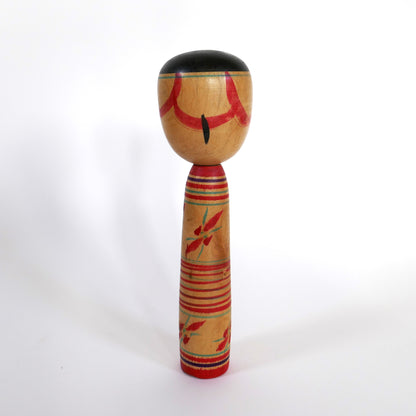 Vue arrière d'une kokeshi japonaise ancienne de Iwamoto Yoshizō – cheveux noirs stylisés et motifs floraux.