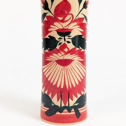 Décor hishigiku 菱菊 sur une kokeshi Naruko traditionnelle, grand chrysanthème stylisé rouge et noir peint sur bois naturel.