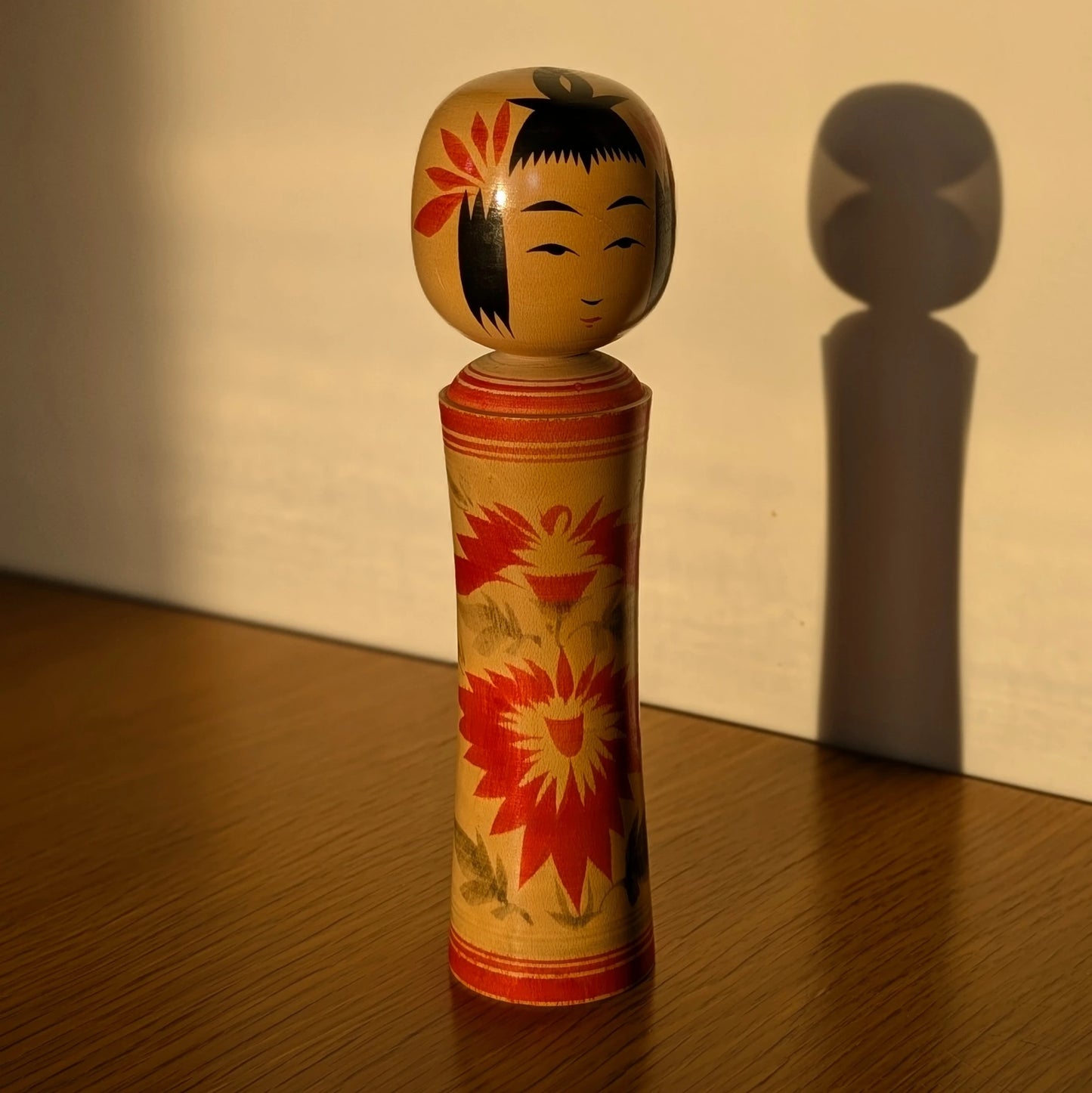 Kokeshi Naruko artisanale de Sato Kazuo en bois, éclairée par une lumière dorée avec ombre portée.