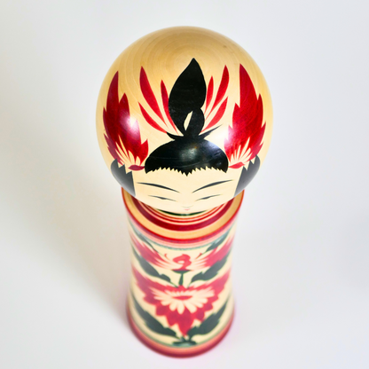 Vue du dessus d’une kokeshi Naruko avec coiffure noire et détails rouges