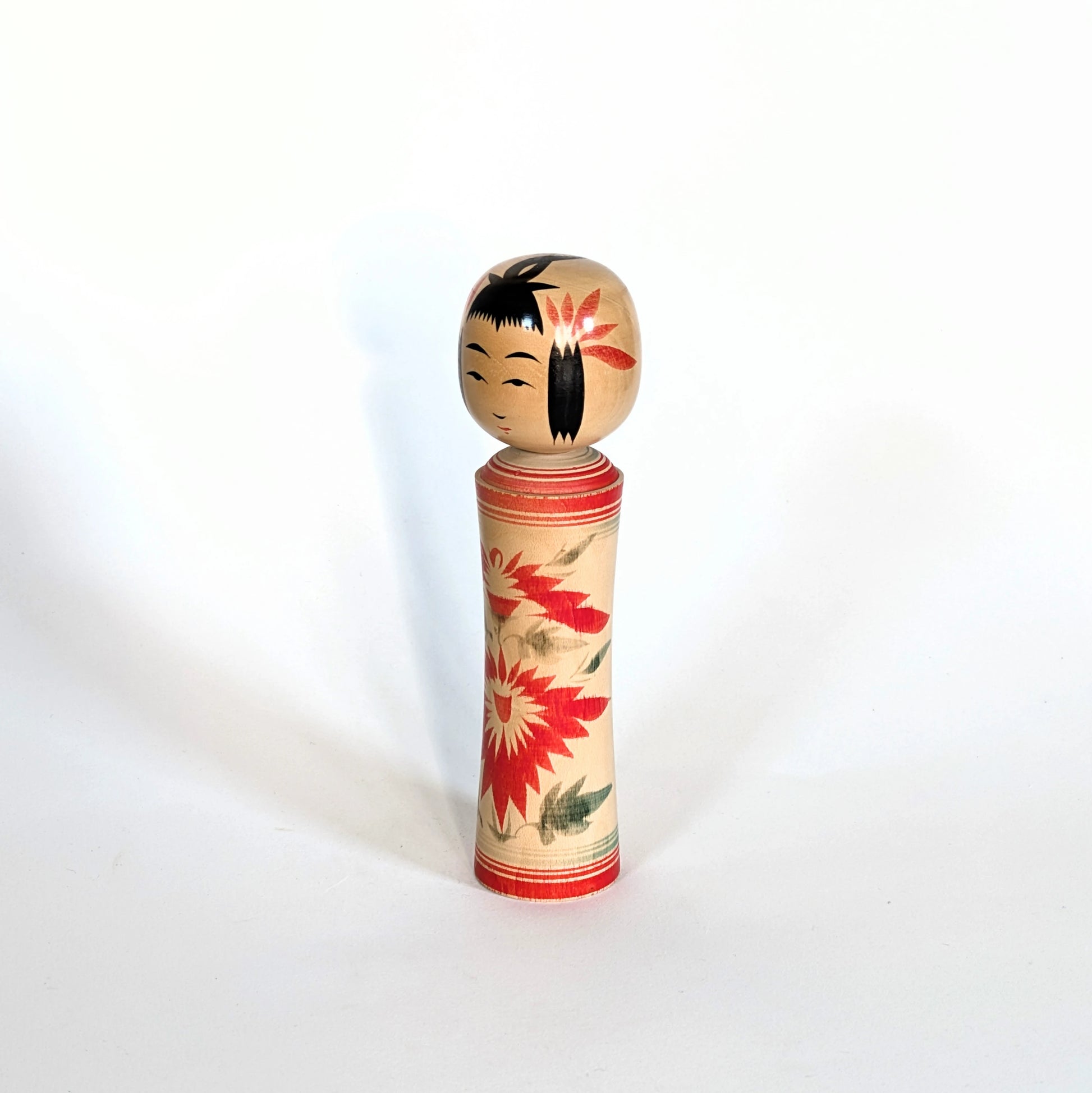 Kokeshi Naruko japonaise en bois décorée de motifs floraux de chrysanthèmes rouges, vue trois-quarts gauche.