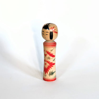 Kokeshi Naruko japonaise en bois décorée de motifs floraux de chrysanthèmes rouges, vue trois-quarts gauche.
