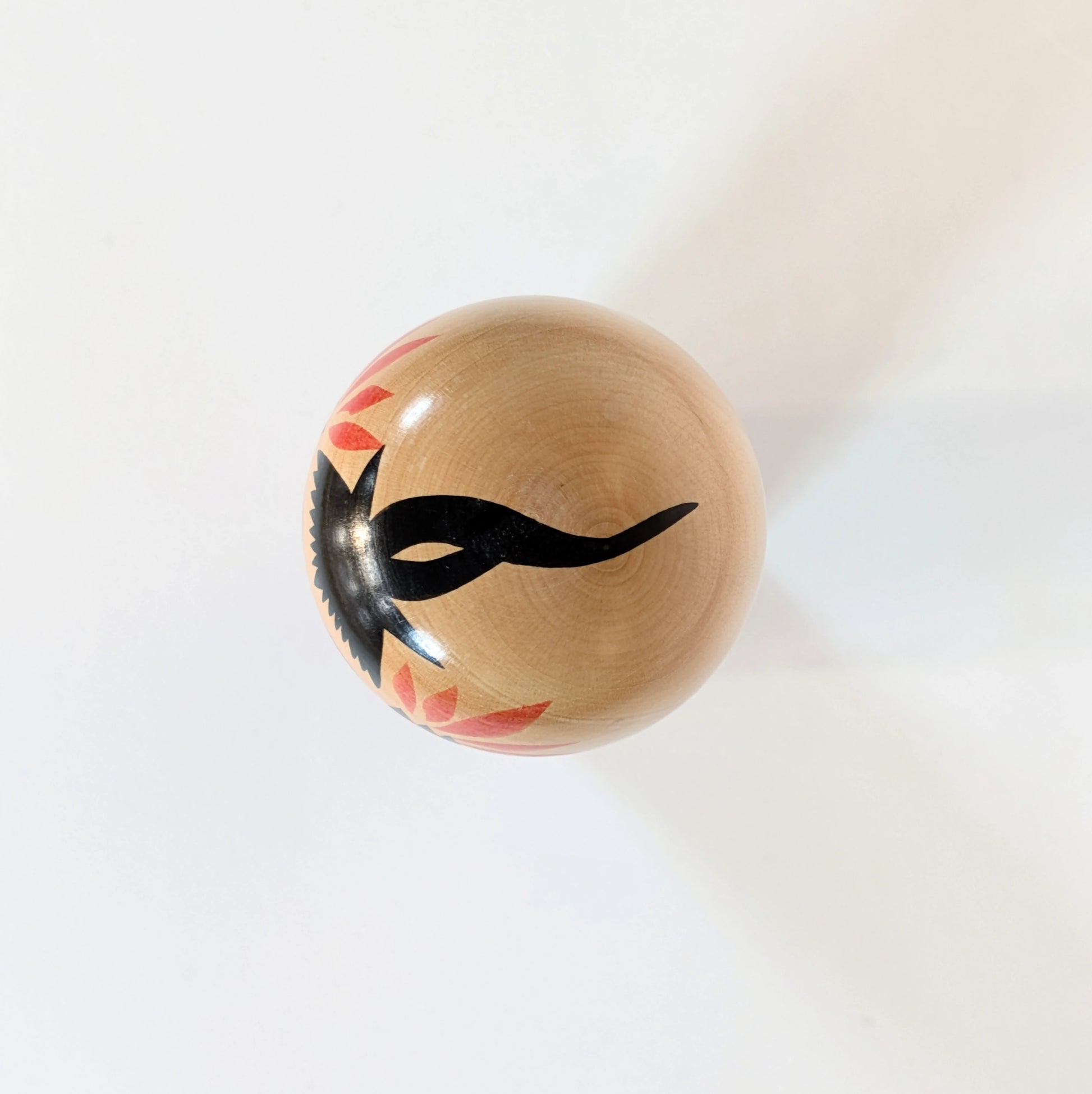 Vue du dessus d’une kokeshi Naruko montrant le motif noir peint sur la tête, représentant la chevelure.