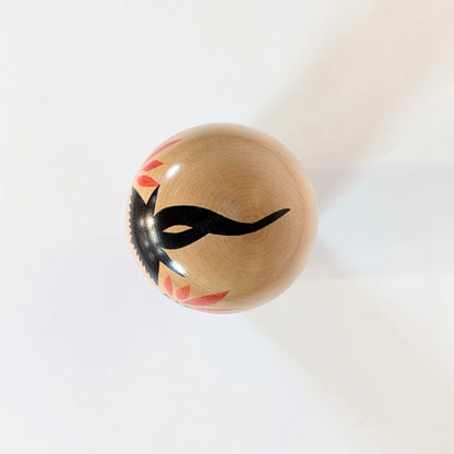 Vue du dessus d’une kokeshi Naruko montrant le motif noir peint sur la tête, représentant la chevelure.