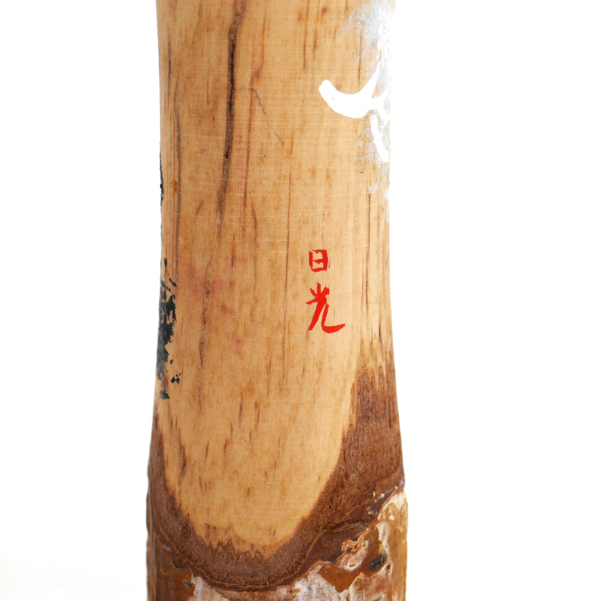 Détail de la signature rouge « Nikkō » sur le tronc en bois naturel d'une kokeshi japonaise.