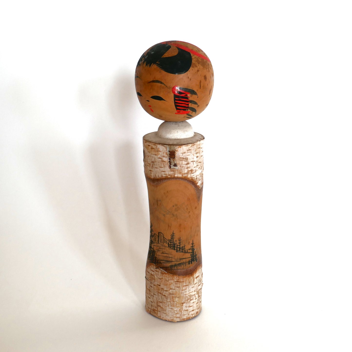 Profil gauche d’une kokeshi omiyage vintage, bois avec écorce et peinture rustique.