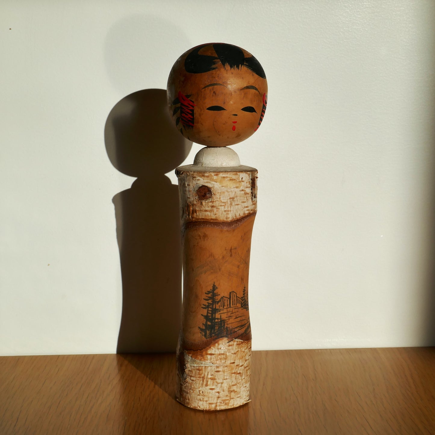 Kokeshi souvenir poupée japonaise en bois naturel photographiée à la lumière du jour, motif de paysage peint, fabriquée à Akakura.