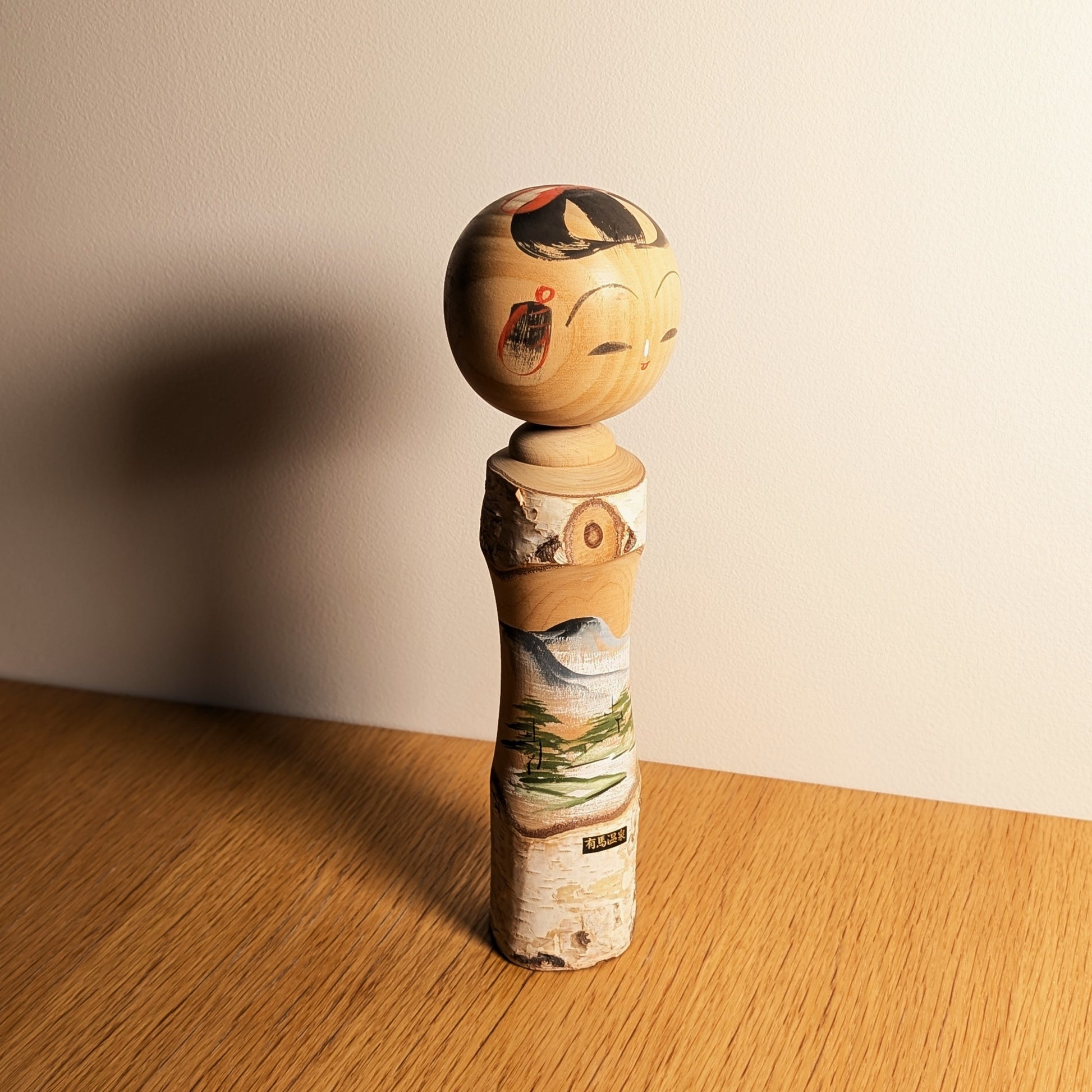 Kokeshi omiyage Arima Onsen en bois naturel, présentée en décoration japonaise avec paysage peint de montagne, rivière et étiquette 有馬温泉