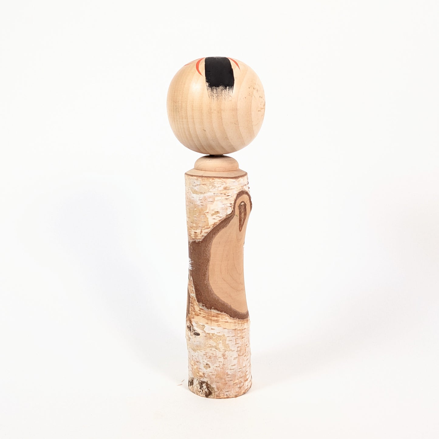 Dos d’une kokeshi omiyage en bois brut avec écorce naturelle, bel exemple d’artisanat populaire japonais