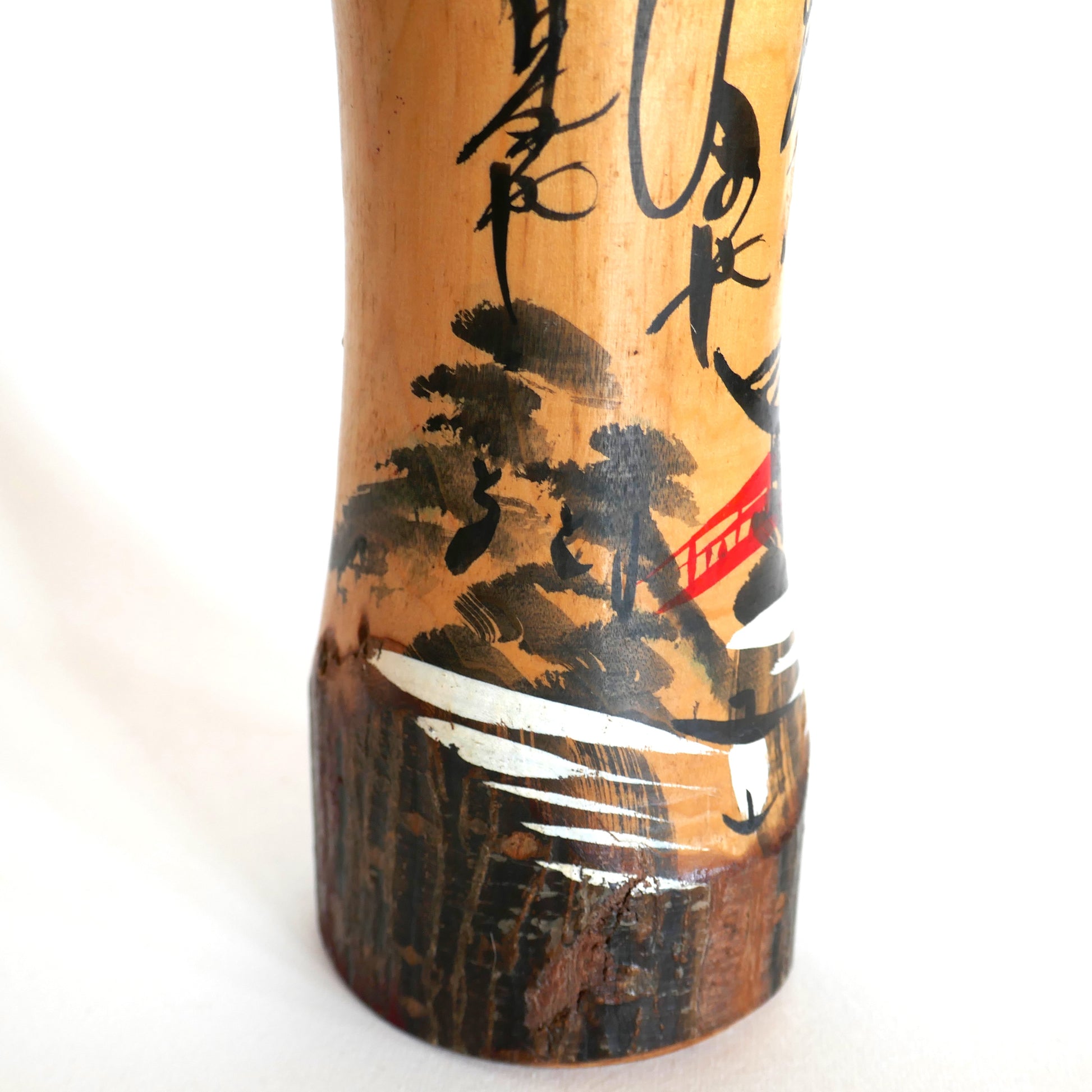 Détail d’un pont rouge dans un paysage peint sur une kokeshi japonaise – style omiyage avec rivière et forêt en lavis d’encre