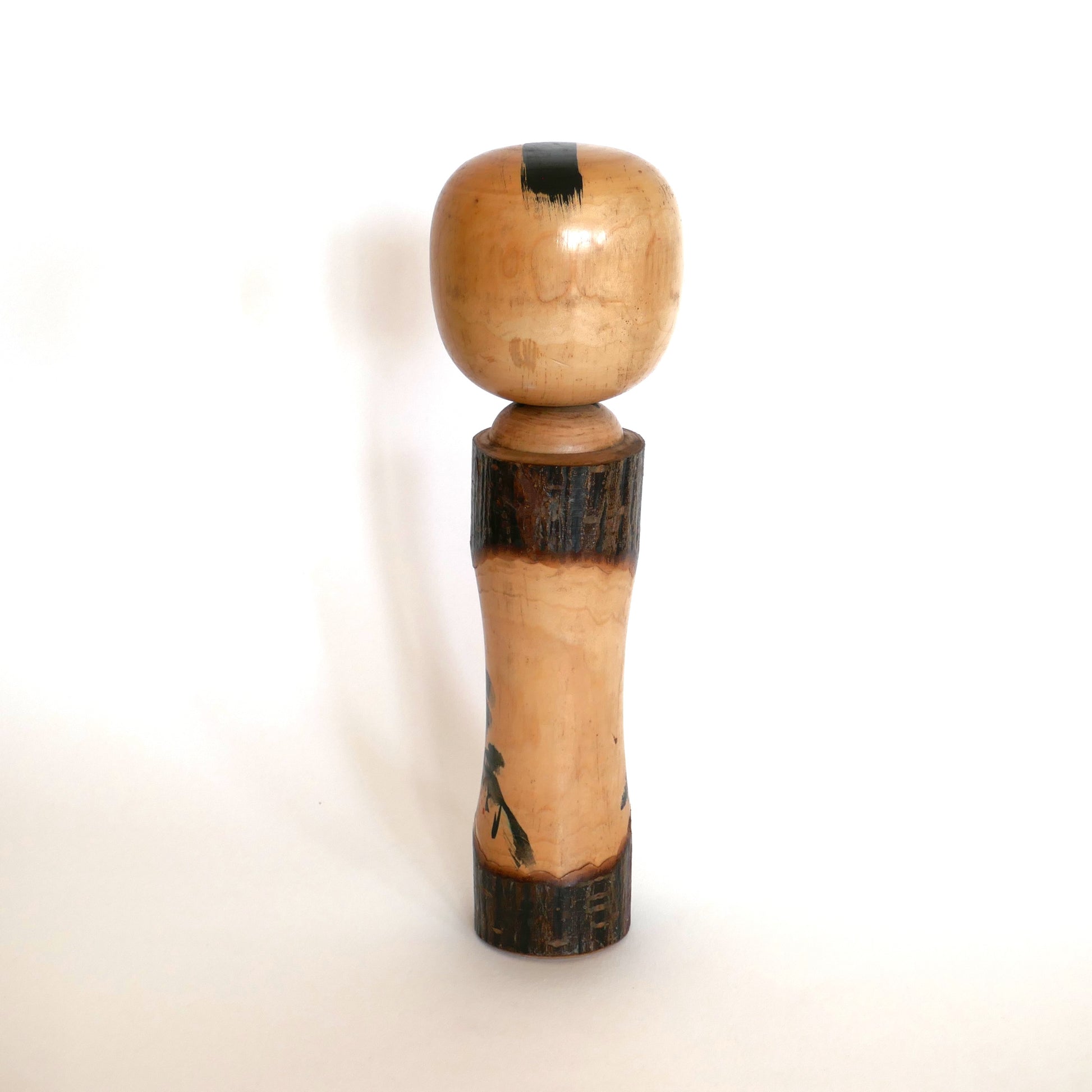 Vue de dos d’une kokeshi japonaise vintage – bois poli et écorce brute sans décor, coiffe noire peinte