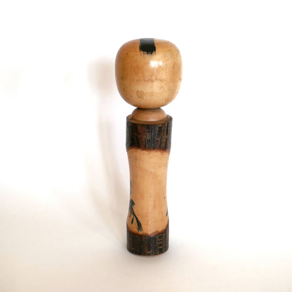 Vue de dos d’une kokeshi japonaise vintage – bois poli et écorce brute sans décor, coiffe noire peinte
