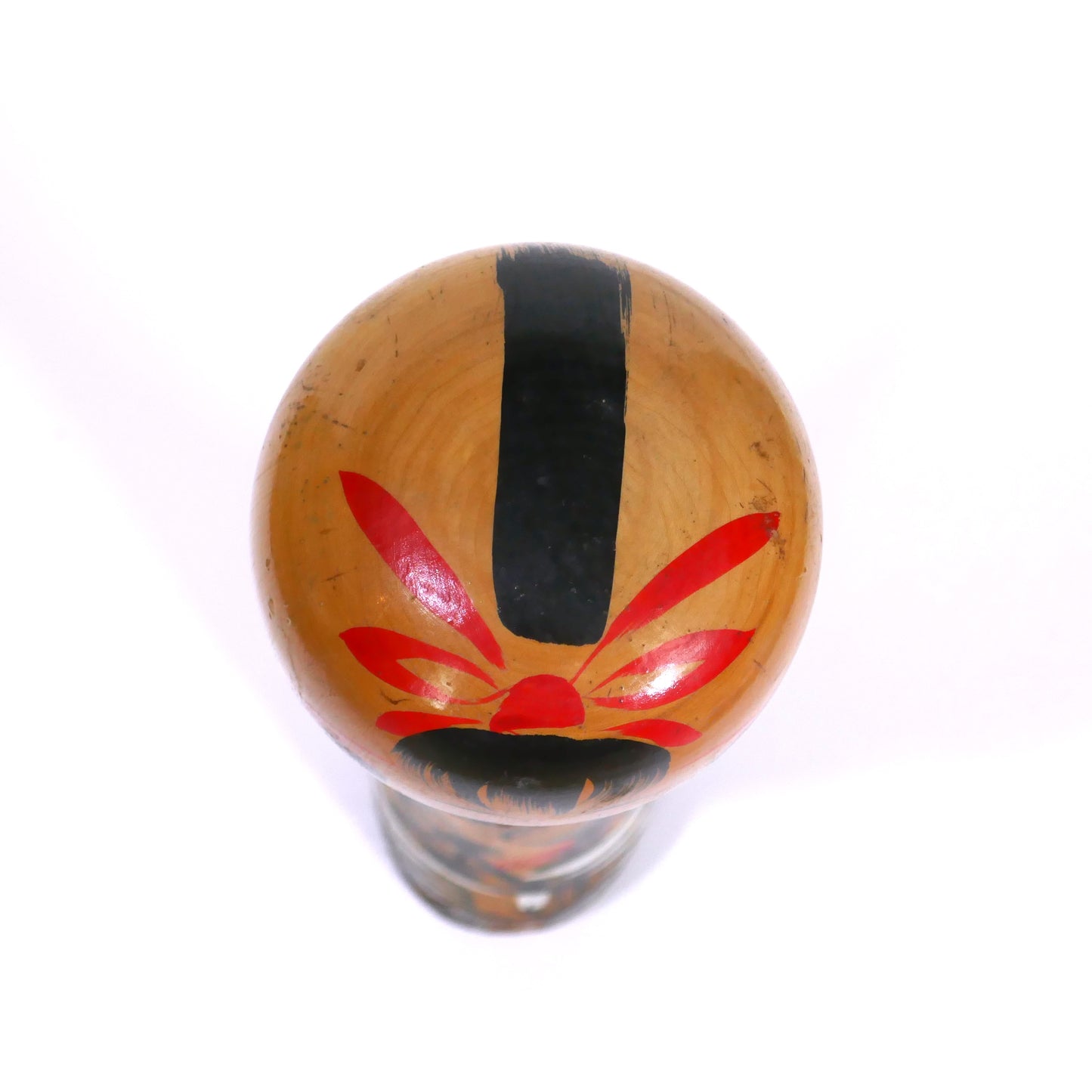 Vue du dessus d’une kokeshi japonaise peinte à la main – coiffe rouge stylisée avec bande noire verticale, style omiyage vintage