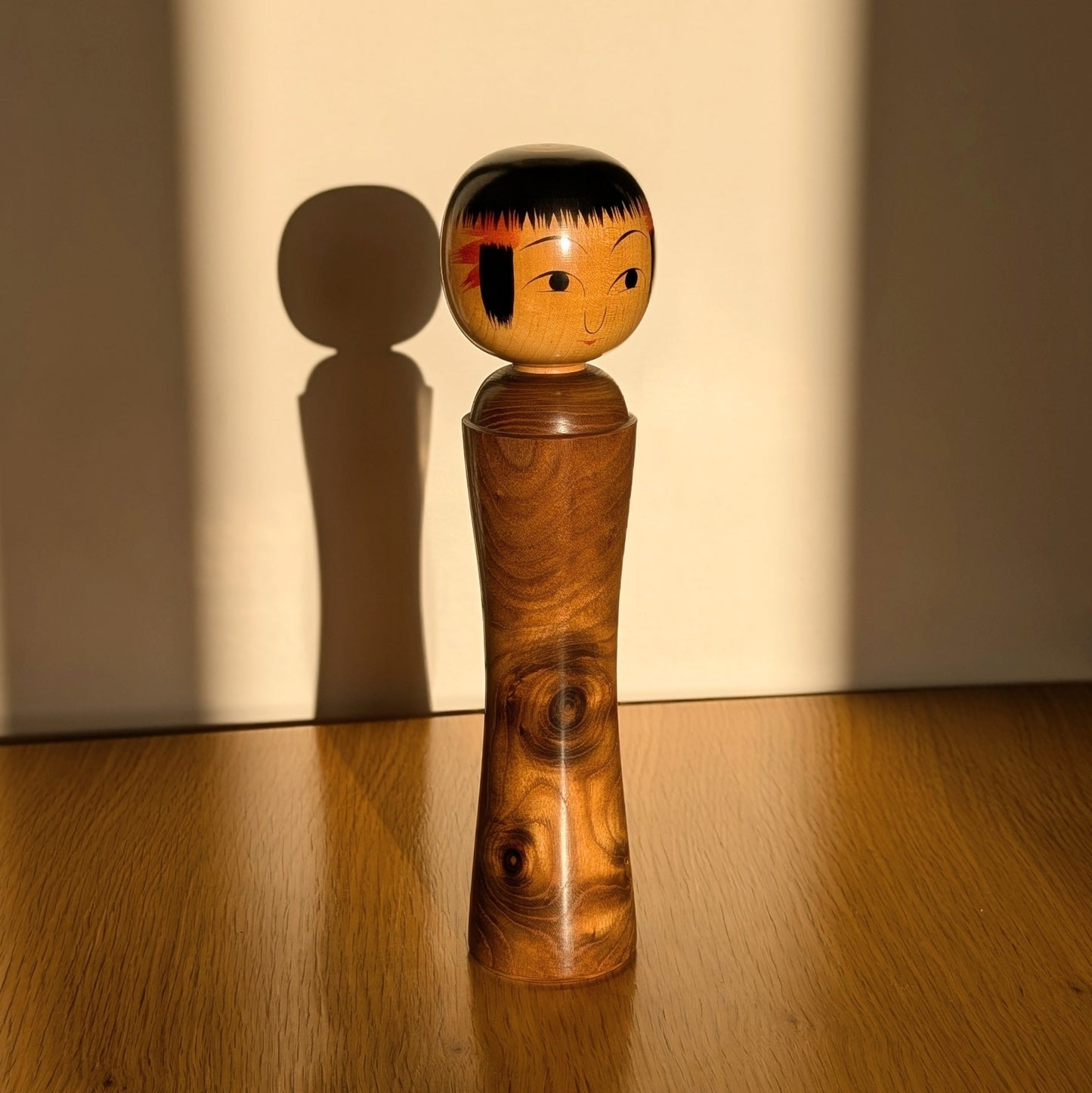 Kokeshi japonaise Oshin dans la lumière du soleil avec ombre portée, artisan Mamoru Izu