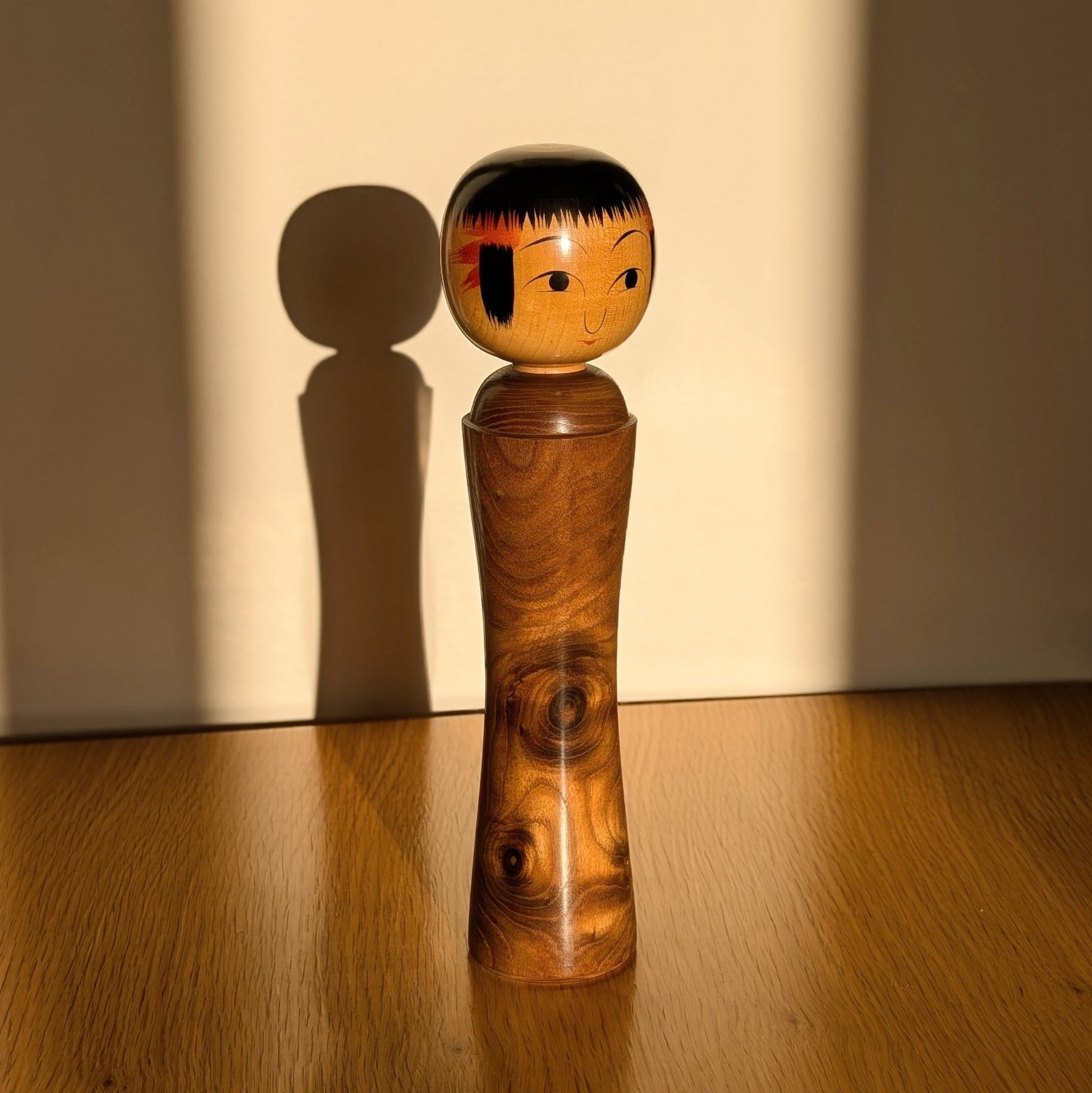 Kokeshi japonaise Oshin dans la lumière du soleil avec ombre portée, artisan Mamoru Izu