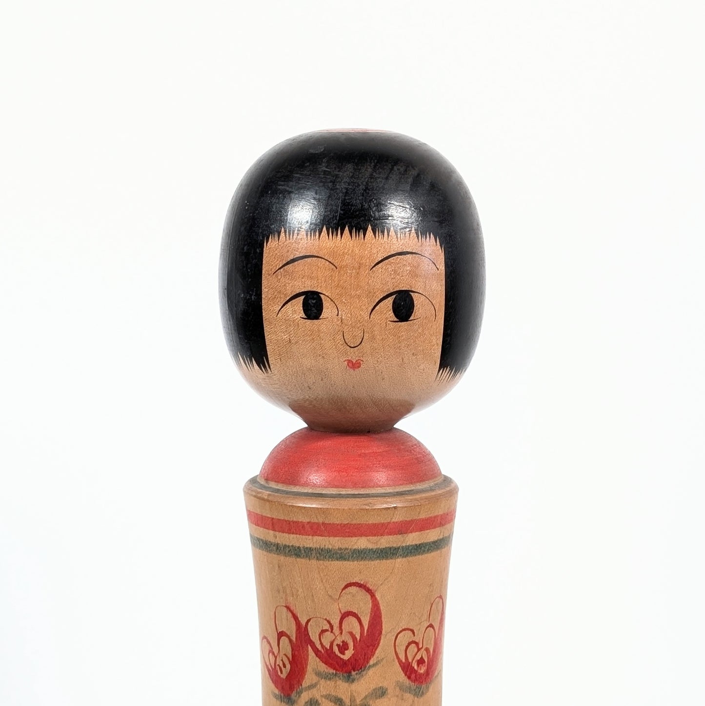 Gros plan du visage d’une kokeshi Oshin par Mamoru Izu, coiffure okappa noire, grands yeux peints et petite bouche rouge